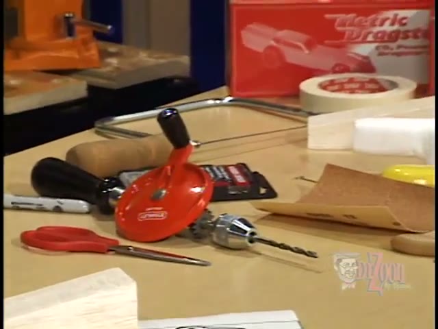 A basswood dragster blank, paper templates, sandpaper, files and a block plane laid out on a bench